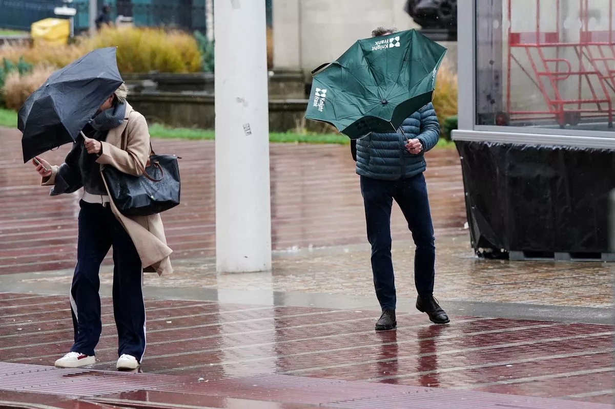 People struggle to hold onto their umbrellas during strong winds in the UK