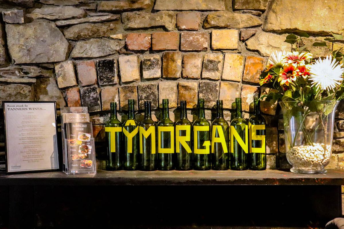 A row of wine bottles. Each is adorned with letters and they spell out 'Ty Morgan'
