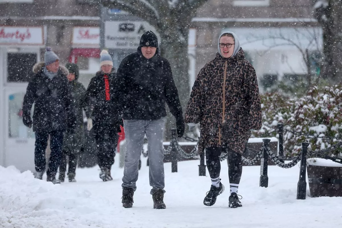 People walk through a snow shower as an 'amber' snow warning is issued on January 02, 2026 in Ballater, Scotland