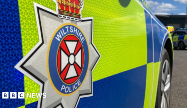 The side of a blue and yellow police vehicle which says 'Wiltshire Police' on the side.