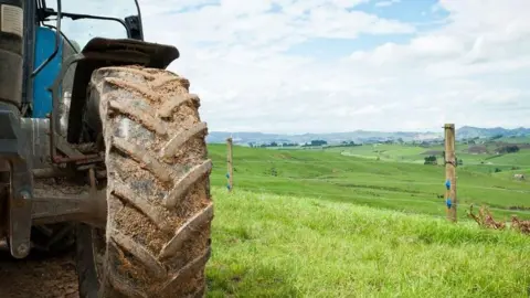 Getty Images A partial picture of tractor focused on the large back wheel on the right hand side with grassy fields in the background