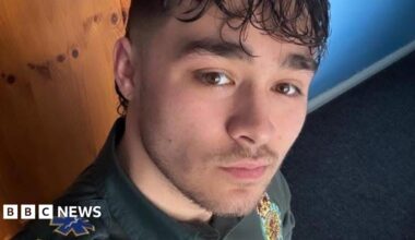 Nico looks into the camera, lips pursed. He has brown eyes and hair and is wearing a green ambulance uniform.