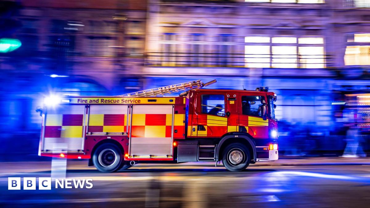 A fire engine drives on an urban road at night with blue lights on.