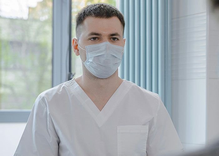Young male doctor wearing a face mask and white coat in a clinical setting, highlighting unprofessional things doctors say.