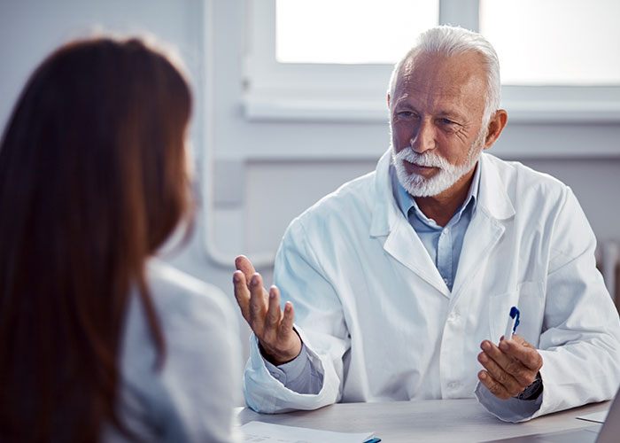 Senior male doctor in white coat talking to a patient in a medical office illustrating unprofessional things doctors say.