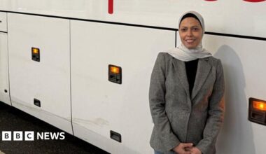 Fatima Benzbir wears a beige jacket, black top and white headscarf, as she leans casually against a coach.