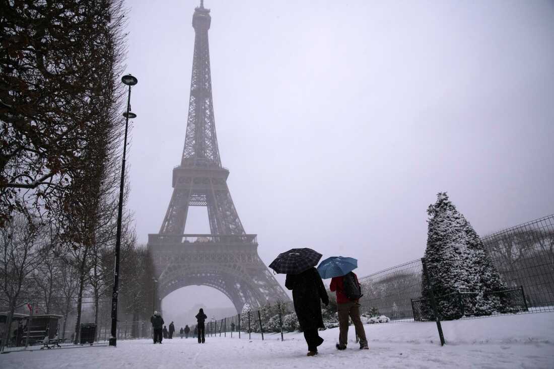 People walk near the Eiffel Tower during a snowfall Wednesday, Jan. 7, 2026 in Paris. 