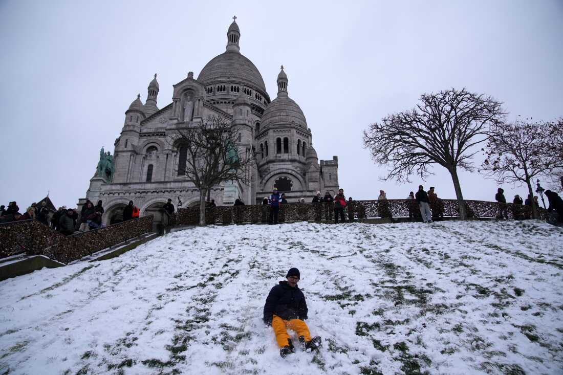 A man plays by the snowy Butte Montmartre with the Sacre-Coeur basilica in background, Wednesday, Jan. 7, 2026 in Paris. 