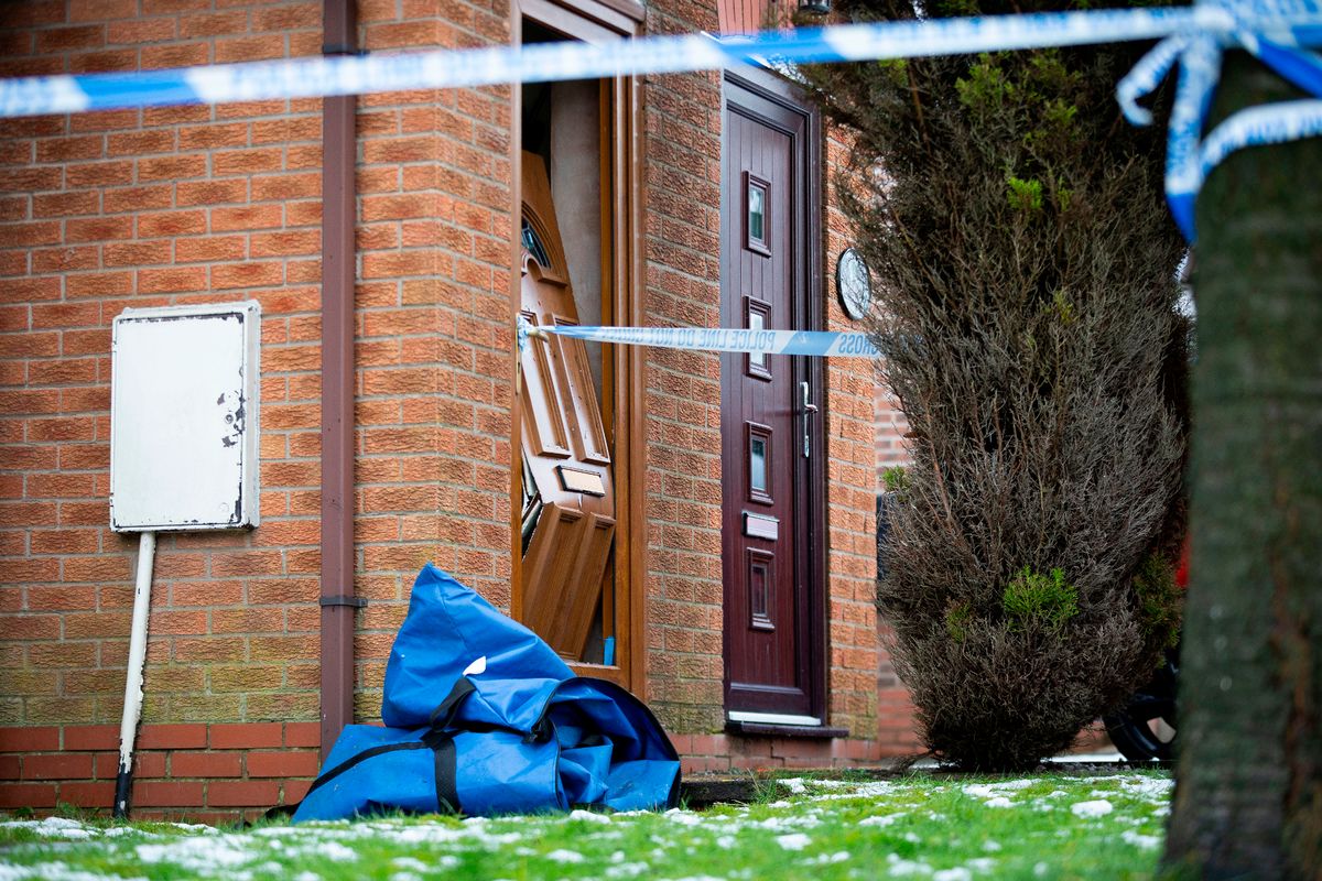 The front door of the house which is off its hinges and leaning against the frame, bent in the middle