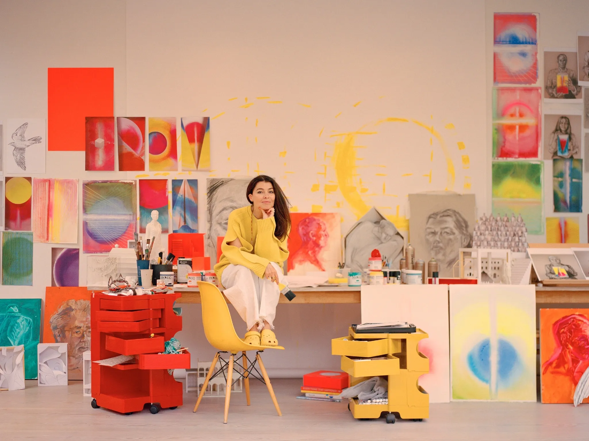 Es Devlin sits on a desk in her London studio surrounded by colourful sketches