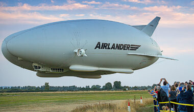 Cargo ship SIMON docked at a busy port, surrounded by shipping containers and cranes under a clear blue sky.