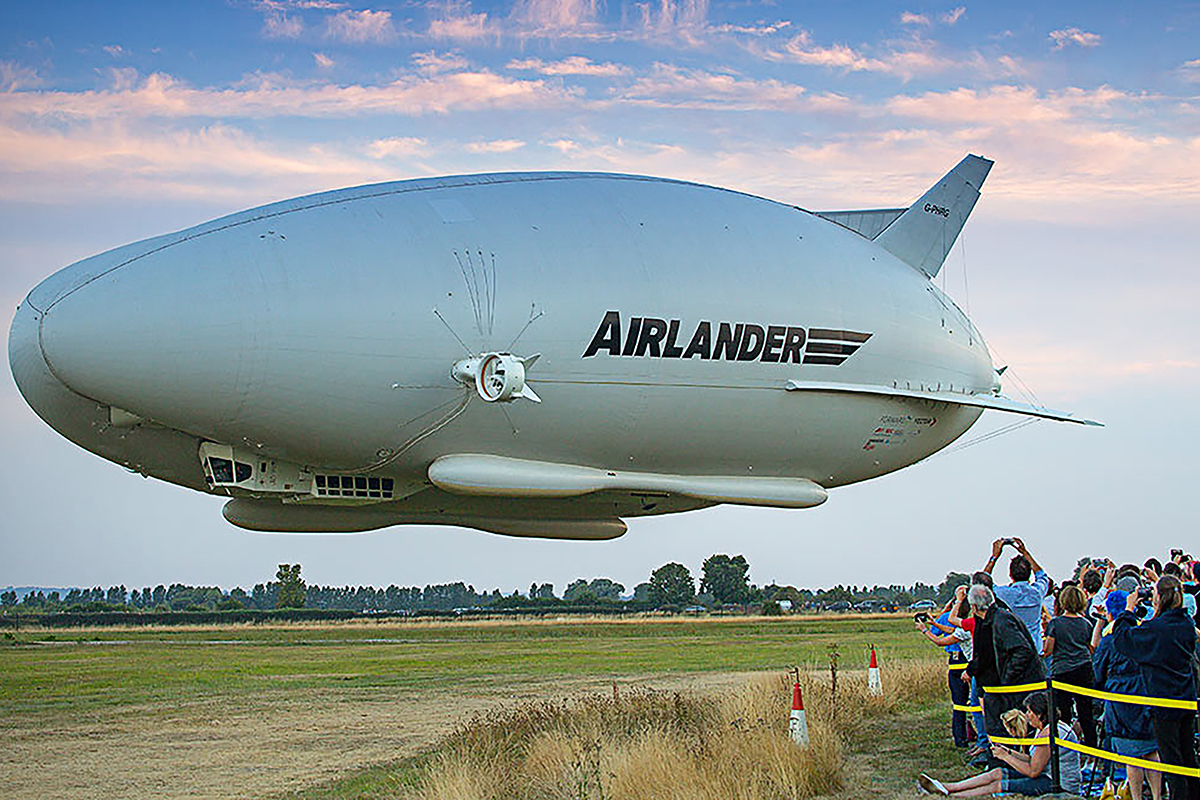 Cargo ship SIMON docked at a busy port, surrounded by shipping containers and cranes under a clear blue sky.