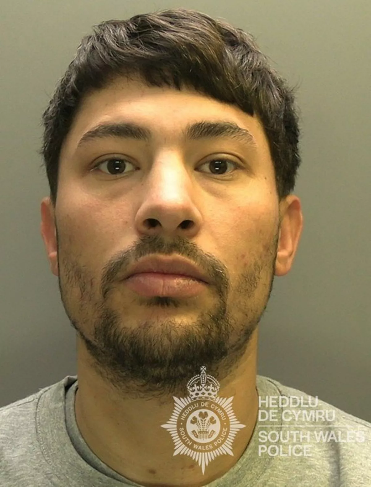Custody photo of Courtney Harris, 32, who has black hair, a black beard and is wearing a grey tracksuit.
