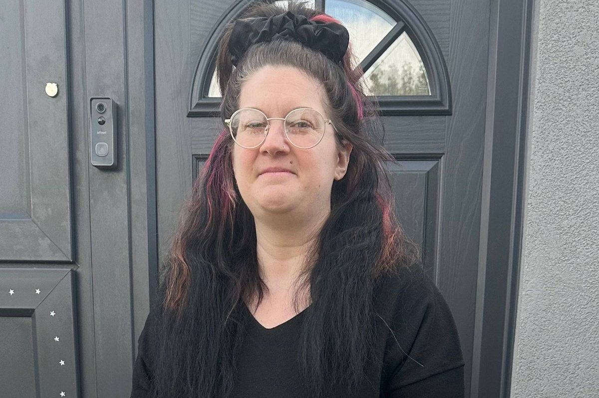An adult female with long hair wearing a black long-sleeved top and brown leggings is standing on crutches in front of a building.