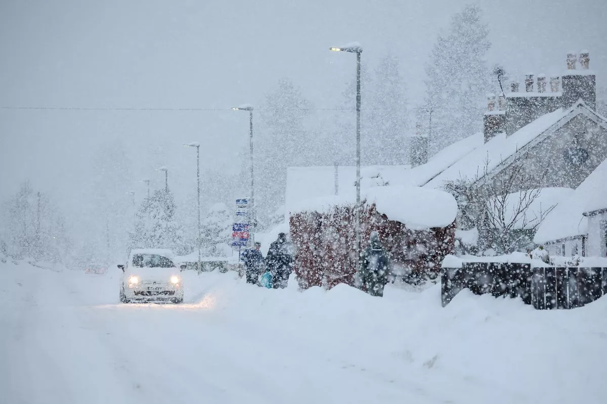 A car drives through the snow as people walk in Main Street Alford as Aberdeenshire Council declared a "major incident"