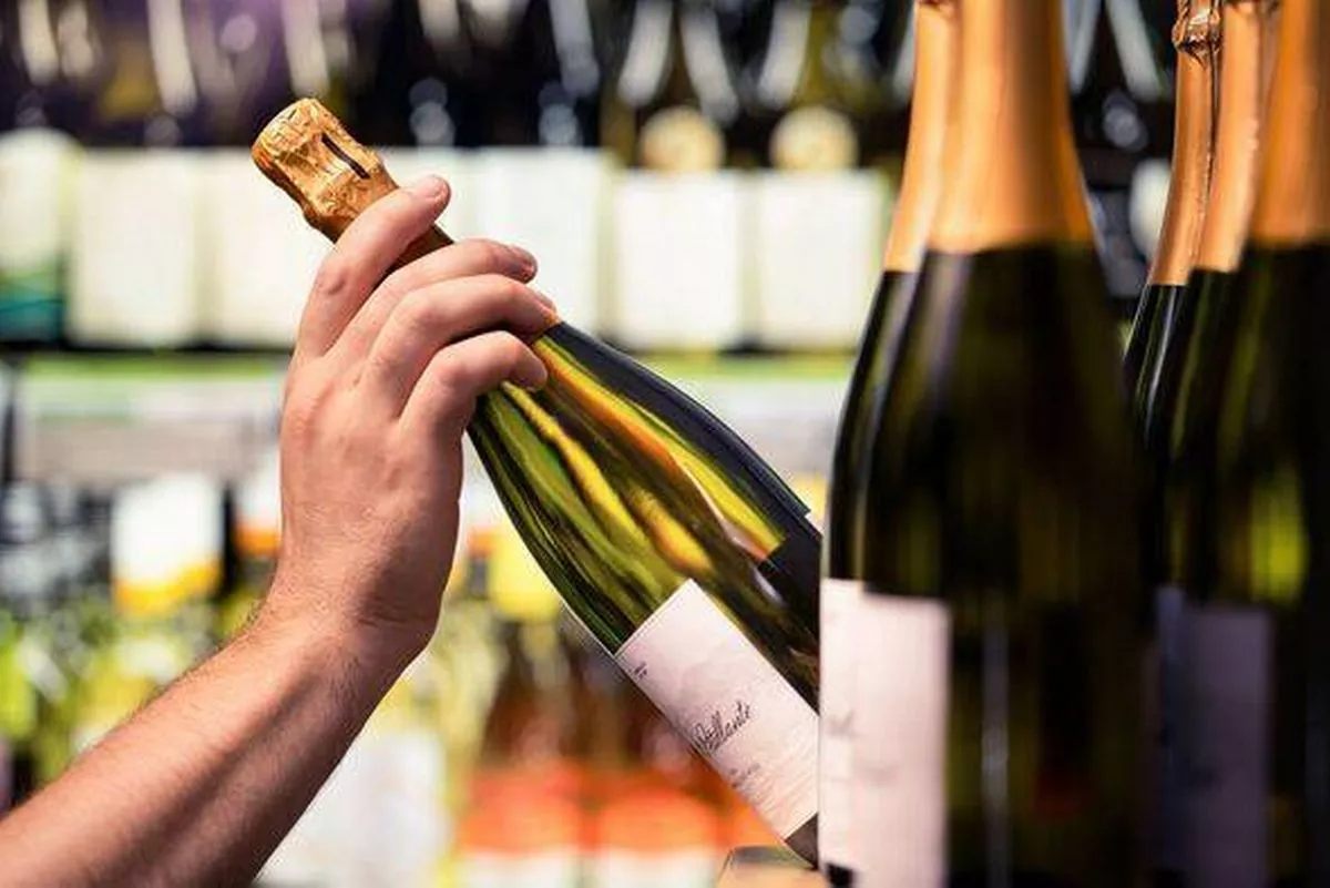 Sparkling wine from shelf of alcohol store. Bottle in hand. Liquor shop. Prosecco or champagne display in spirits market or supe
