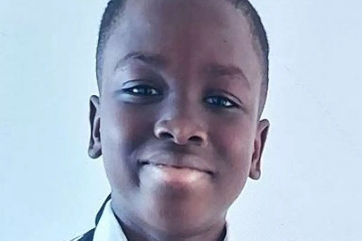 A little boy smiling and wearing uniform. He has black skin and short black hair