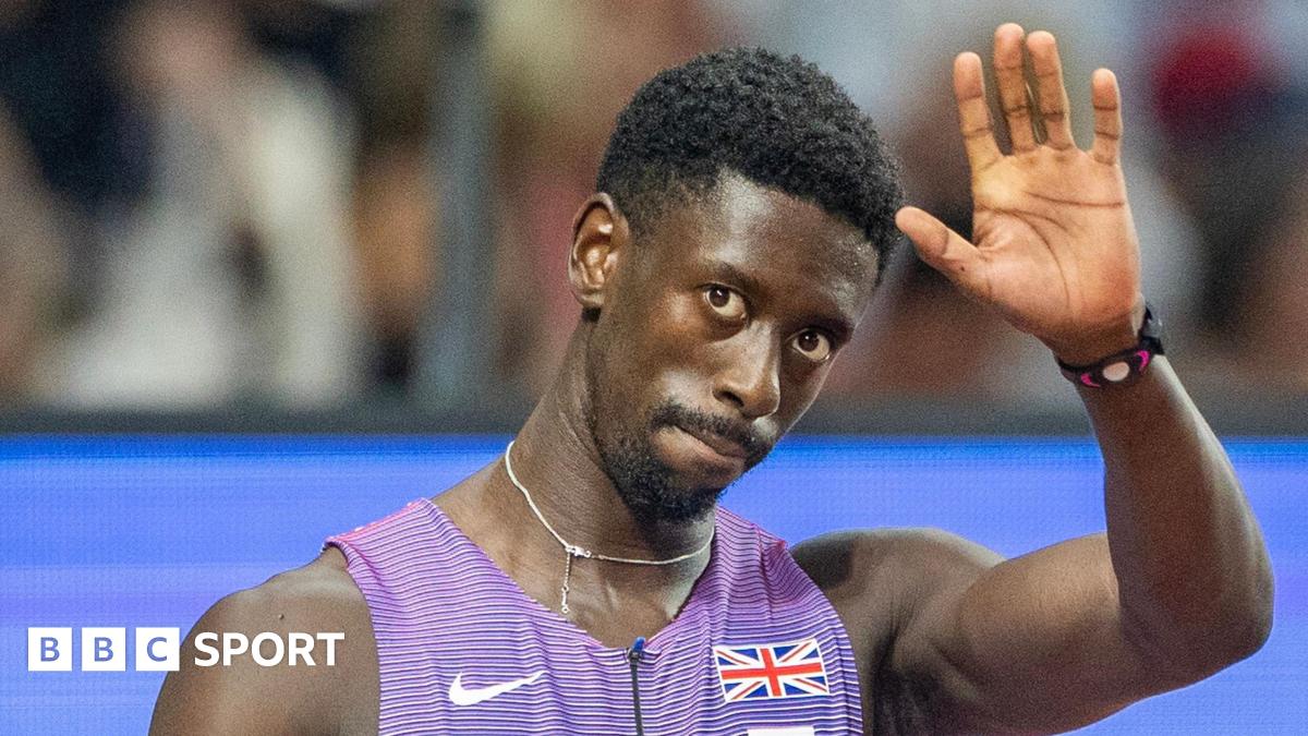 Former Great Britain sprinter Reece Prescod waves with his left hand as he wears purple and white kit with a union jack badge and Nike swoosh logo on the front