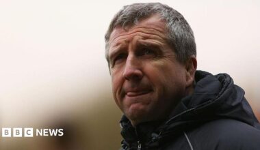 A grey haired man in a black coat, with a look of concentration staring off into the distance.
