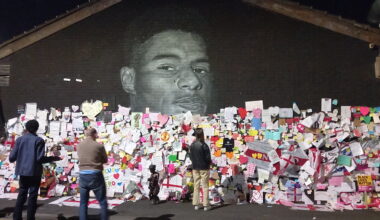 A black wall with a mural of the face of footballer Marcus Rashford on it, the wall is covered in thousands of pieces of paper in all colours, shapes and sizes