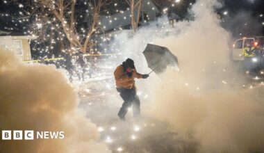 A protester on a snowy street uses an umbrella to shield themself from a cloud of tear gas and sparks in Minneapolis
