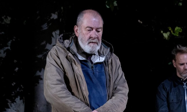 Bear stands beside a freshly dug grave with Celia and Ray in the background in Emmerdale