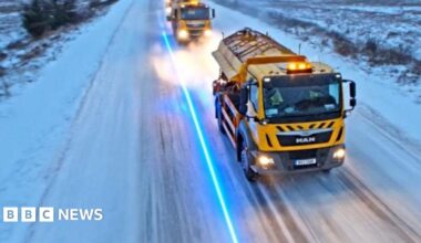 Yellow gritters travelling down a road in Lancashire covered in snow and ice.