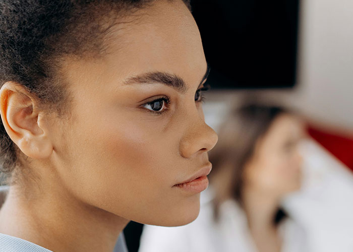 Close-up of a thoughtful young woman with a blurred doctor in the background, highlighting unprofessional things doctors say.