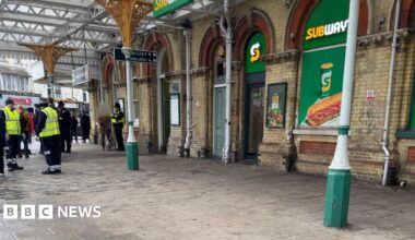 The outside of a railway station. There is a large yellow and green Subway signages displayed on the windows.