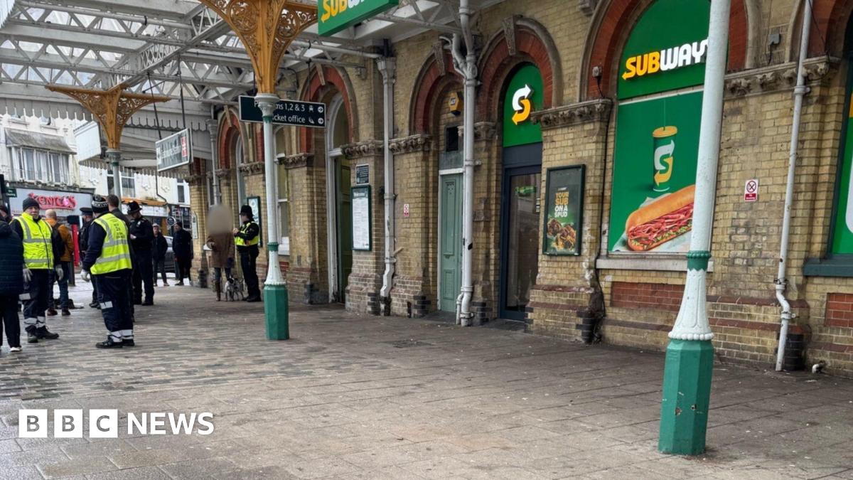 The outside of a railway station. There is a large yellow and green Subway signages displayed on the windows.