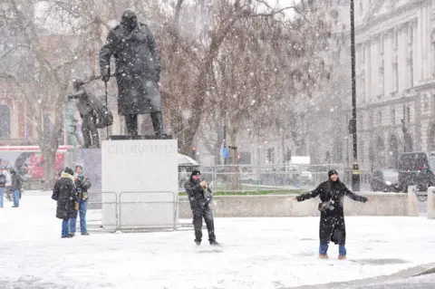 PA Media People dance in the snow in front of Winston Churchill's statue in Parliament Square, Westminster.