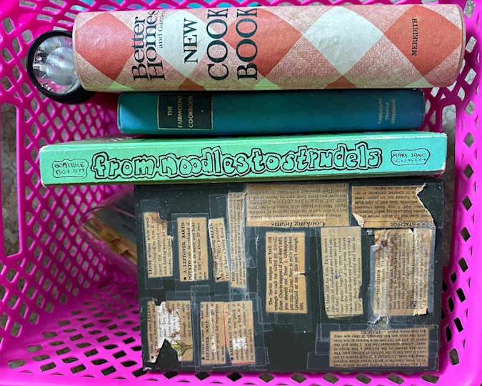 A pink basket containing various cookbooks, including 