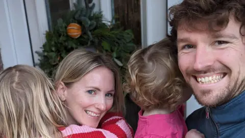 Louise and Pete smile at the camera, holding their two daughters