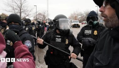 a Customs and Border Patrol agent holding up a baton as more agents gather behind him