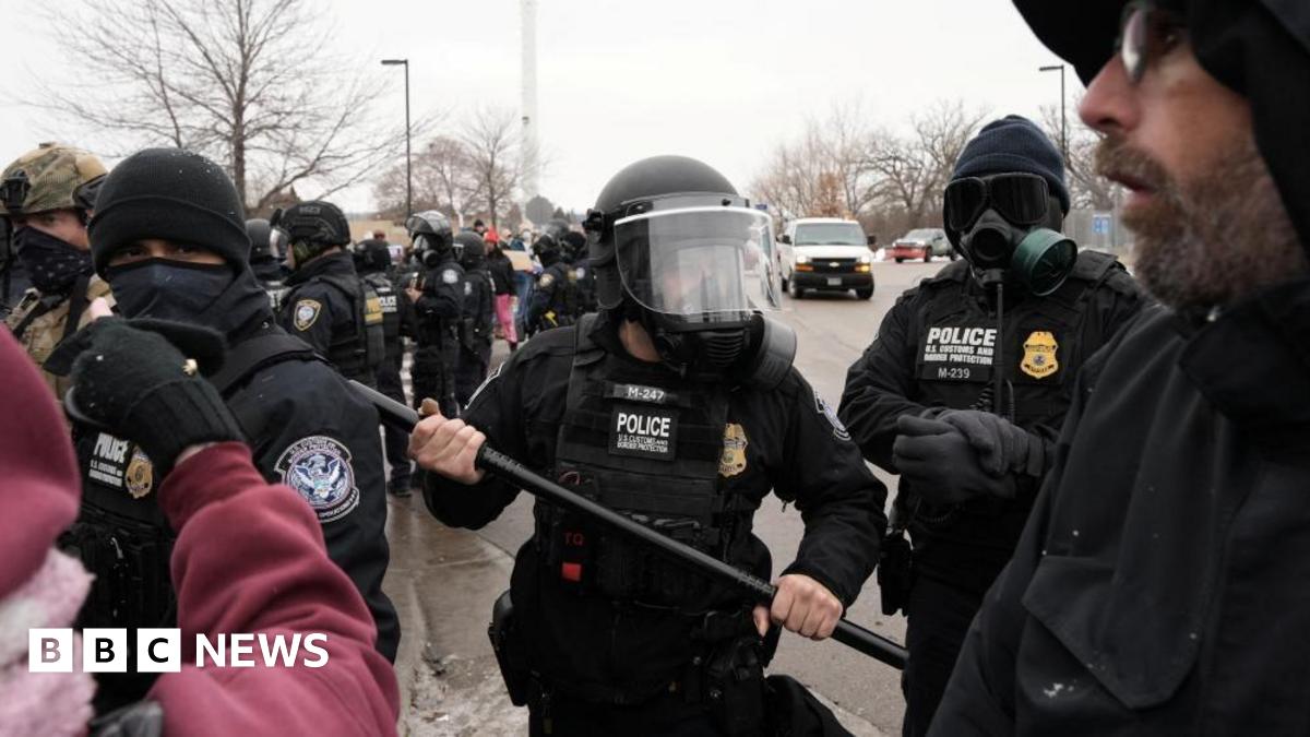 a Customs and Border Patrol agent holding up a baton as more agents gather behind him