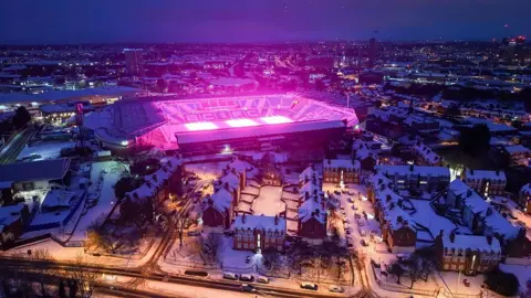 Getty Images An aerial view of Birmingham City Football Club ground, St Andrews. It is surrounded by snow-covered buildings in the city centre and the pitch can be seen lit up in a bright pink colour