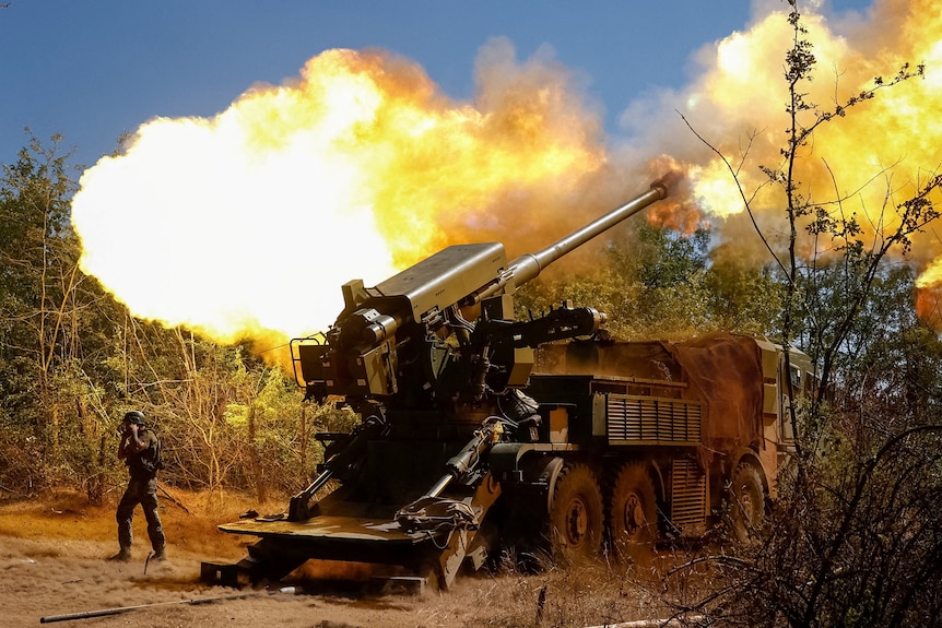 A large military howitzer firing a round in the middle of scrubland.