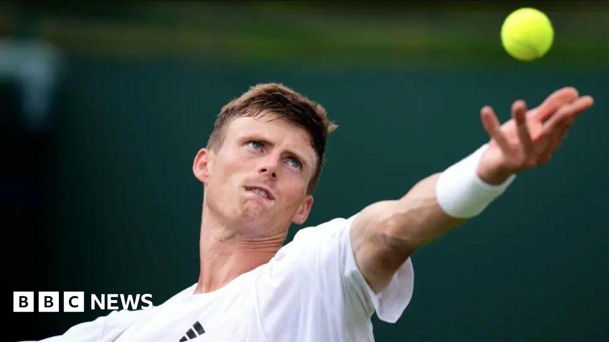 Harris, serving at Wimbledon - his arm is outstretched and his eyes are fixed on the yellow ball in the air. He is wearing white and has short brown hair.