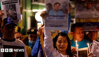 A group of protesters with a woman centred hold candles and signs of people who have been made political prisoners in Venezuela