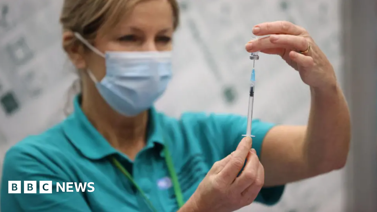 A woman is wearing a blue mask while holding a syringe.
