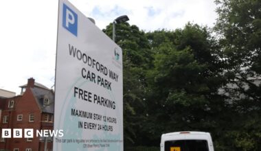 A close-up shot of a sign that reads: 'Woodford Way car park. Free parking. Maximum stay 12 hours in every 24 hours.'