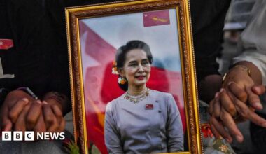 A picture of detained civilian leader Aung San Suu Kyi is seen as Myanmar migrants living in Thailand hold hands during a memorial in Bangkok on March 4, 2021 to honour those who died during demonstrations against the military coup in their homeland.