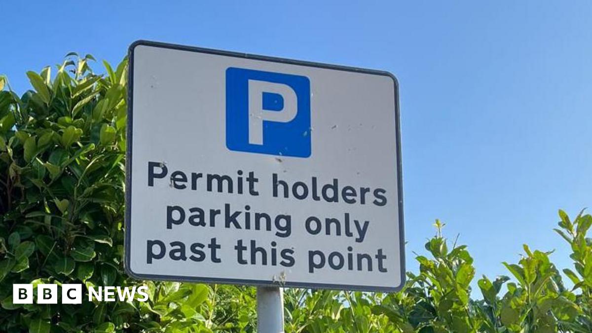 Rob standing in front of a field in a residential area. He is wearing a dark jacket and black rimmed glasses and is smiling at the camera.