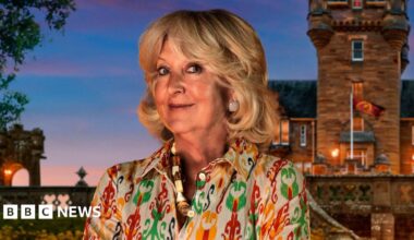 Handout photo of Fiona, one of the contestants in series four of BBC1's The Traitors. Fiona has short blown curled hair, blue eyes and smiles at the camera. She wears a yellow, green and red patterned blouse, a thick shell necklace and diamond earrings. A UGC image of the castle is seen in the background.