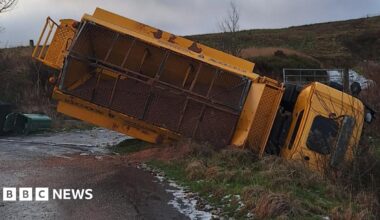 An overturned gritting lorry stuck in a ditch off a road on great, icy, wet moorland countryside