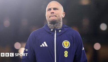 Lyndon Dykes standing in a Scotland training top, with wireless headphones in his ears