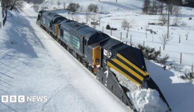 A train with a snow plough attached trundling through a snow-bound landscape