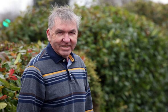 Man in a grey and blue striped shirt by green bush