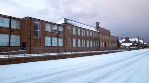 A brown stone school building with snow outside
