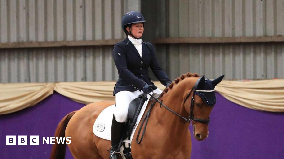 A woman riding a brown horse inside. She is wearing a helmet and a black coat, and boots.